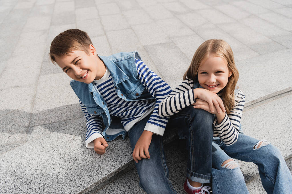 high angle view of happy and well dressed children sitting on stairs in urban street  - Foto, Imagen