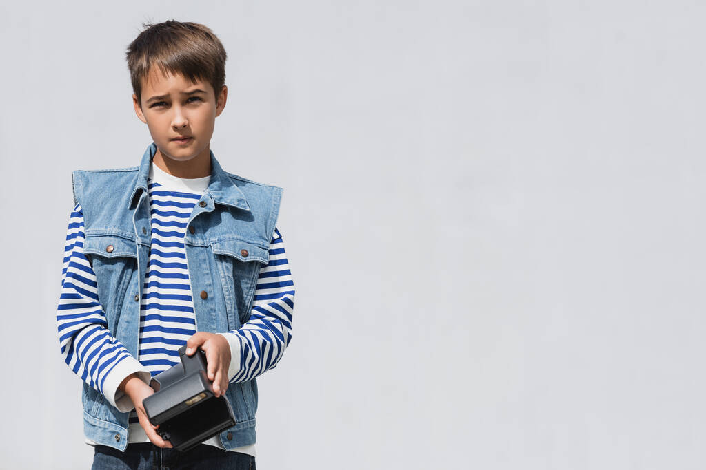 well dressed preteen boy in denim clothes holding vintage camera on grey background   - Foto, imagen