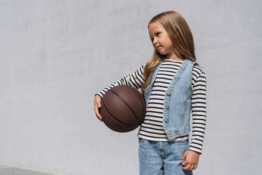 preteen κορίτσι σε denim γιλέκο και μπλε τζιν κρατώντας μπάσκετ κοντά στο εμπορικό κέντρο κτίριο  - Φωτογραφία, εικόνα