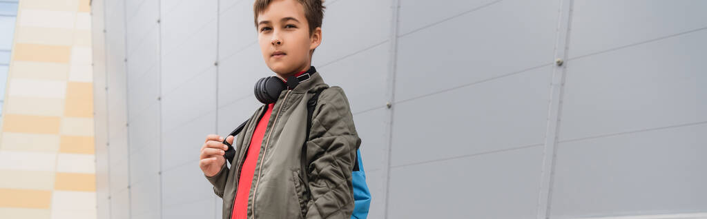 preteen boy in wireless headphones standing with backpack near mall, banner  - 写真・画像
