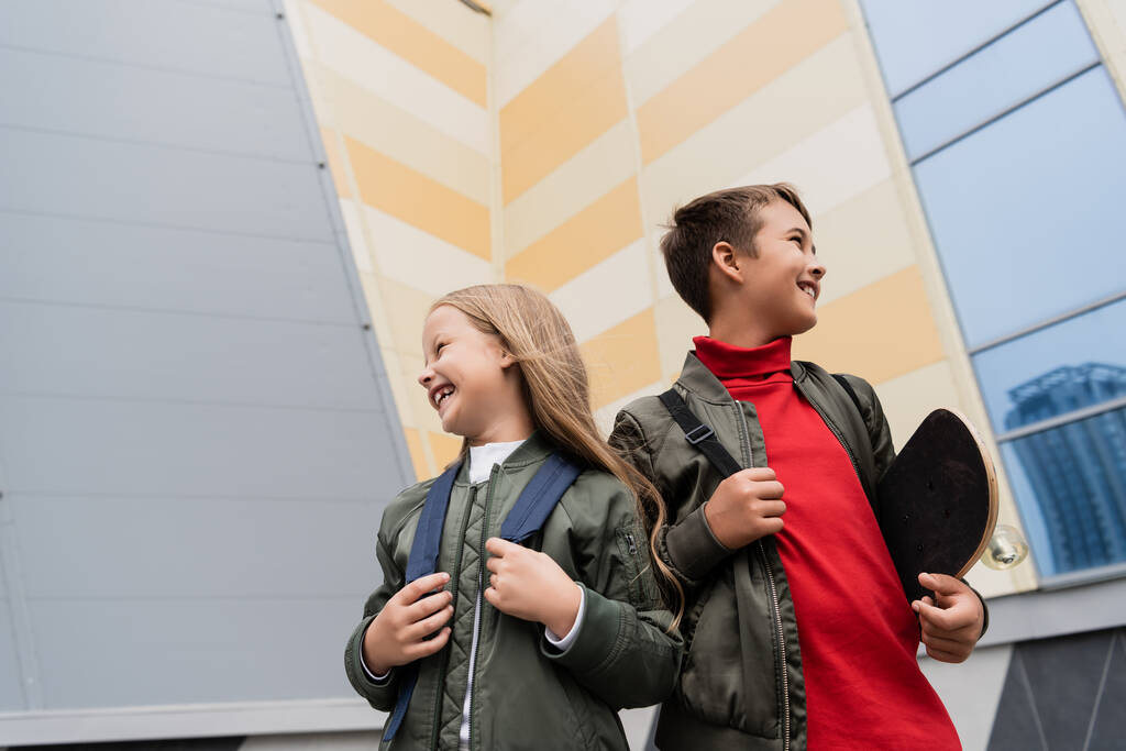 alacsony szög kilátás boldog tizenéves fiú kezében penny fórumon, miközben áll a lány közelében bevásárlóközpont  - Fotó, kép