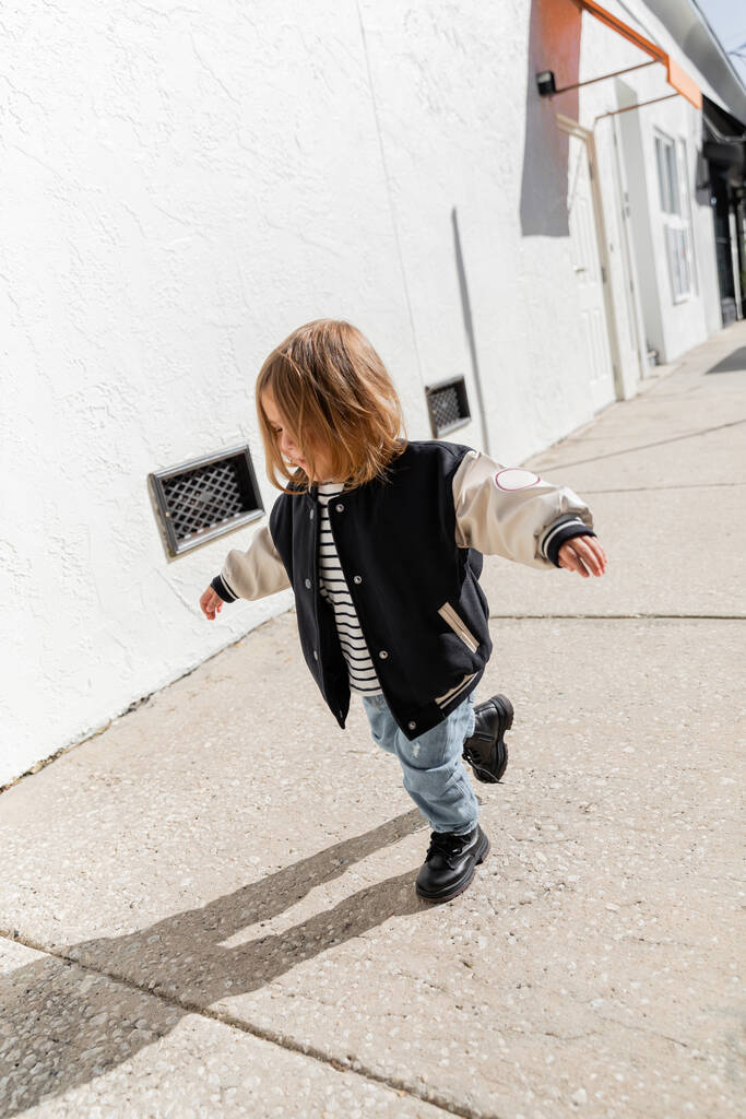 tutta la lunghezza della bambina in giacca bomber elegante che cammina per strada a Miami  - Foto, immagini