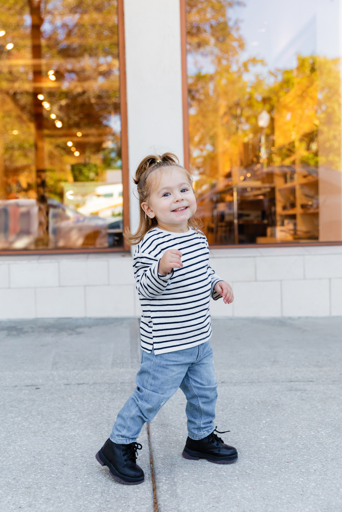 longitud completa de chica feliz en jeans y camisa de manga larga de pie cerca de escaparate de la tienda en Miami  - Foto, Imagen