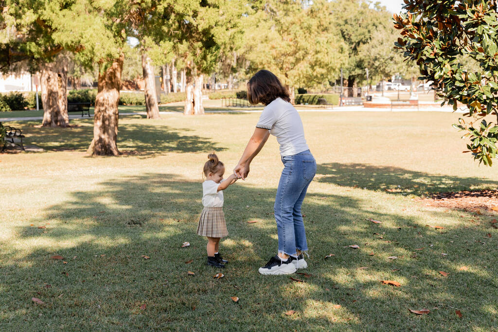 pełna długość matki w dżinsach trzymając się za ręce z córką malucha w parku Miami  - Zdjęcie, obraz