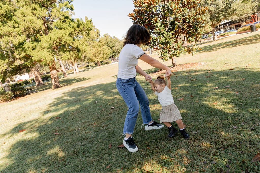 donna bruna che si tiene per mano con allegra bambina mentre gioca nel parco di Miami  - Foto, immagini