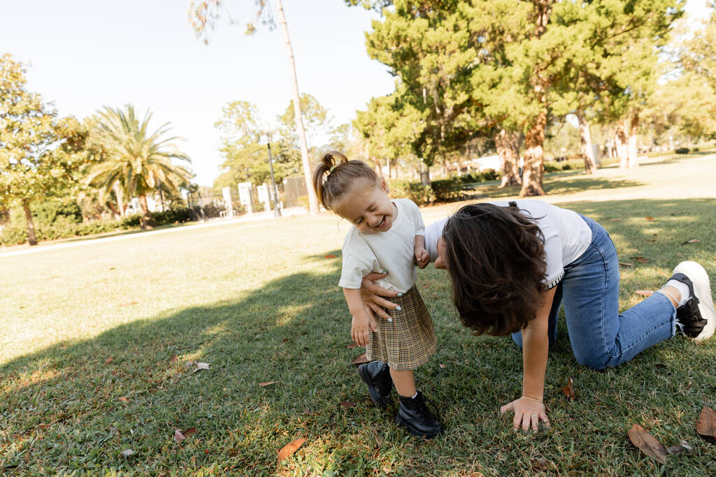 peuter meisje lachen in de buurt van moeder terwijl samen spelen in Miami park  - Foto, afbeelding