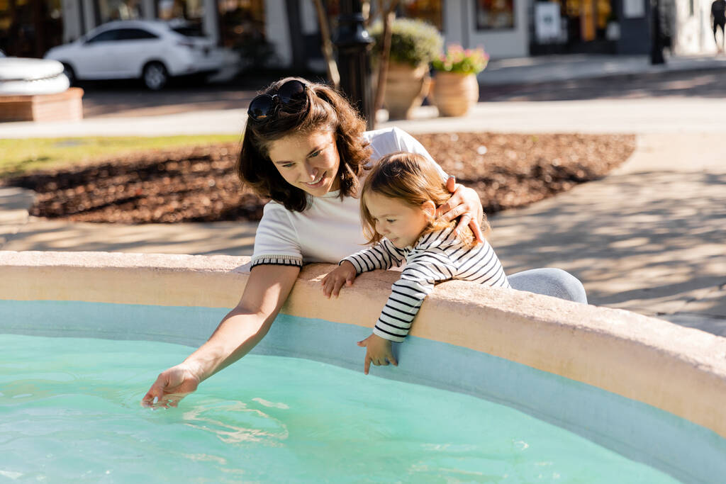 mère heureuse regardant l'eau claire dans la fontaine près de sa fille à Miami  - Photo, image