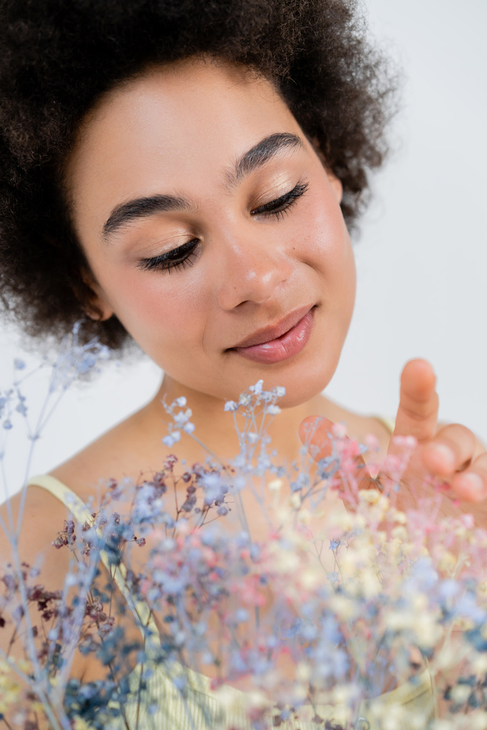 Портрет молодої афроамериканки з натуральною гривою торкається квіток з диханням, ізольованих на сірому.  - Фото, зображення
