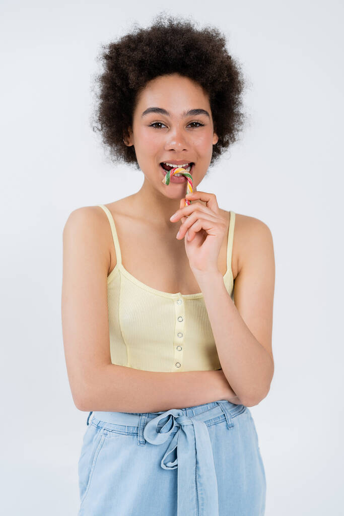 Modelo afroamericano sosteniendo colorido bastón de caramelo aislado en gris  - Foto, imagen