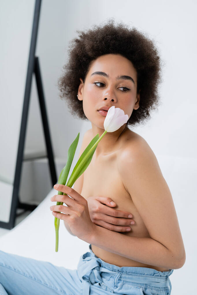Αφροαμερικανή γυναίκα με γυμνό στήθος που κρατά τουλίπα σε γκρι φόντο - Φωτογραφία, εικόνα