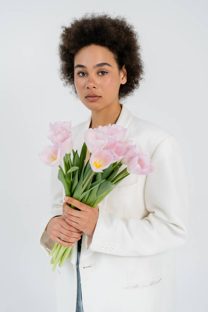 African american model in jacket holding bouquet of tulips isolated on grey  - Photo, Image
