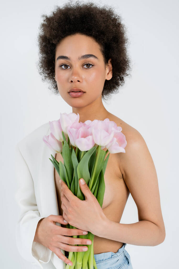 African american woman with jacket and flowers looking at camera isolated on grey  - Photo, Image