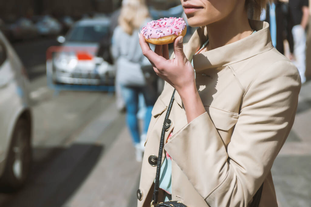Dag schot van jonge vrouw met donuts in haar handen op straat - Foto, afbeelding