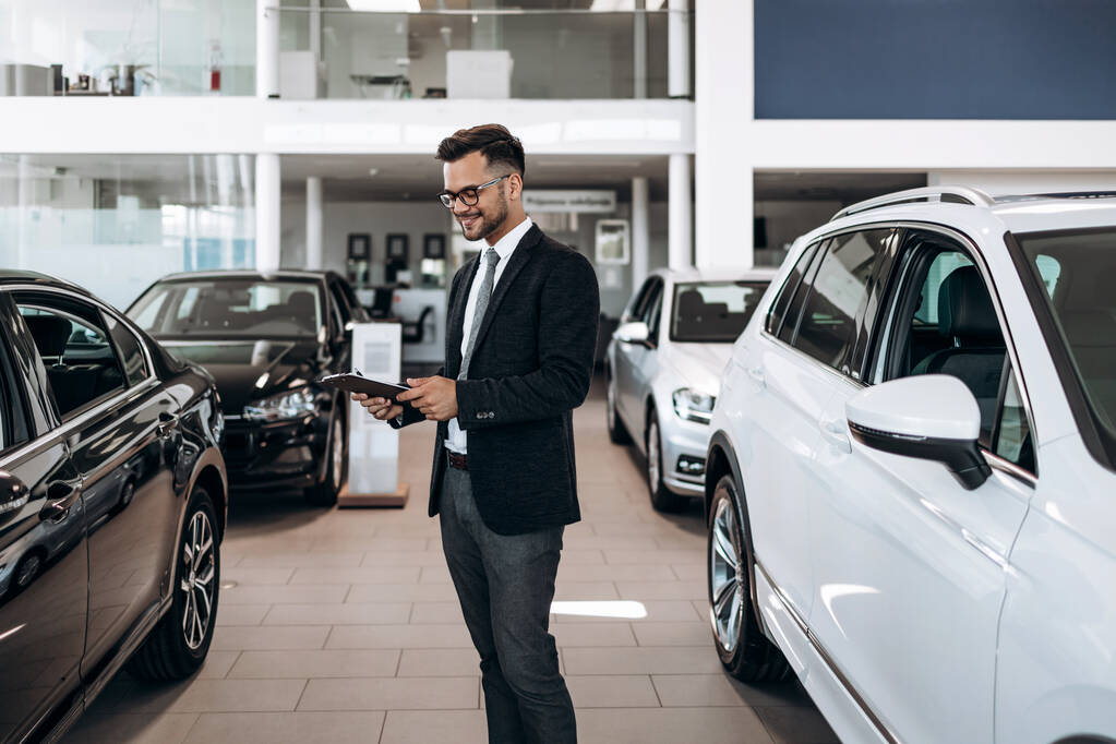 Good looking, cheerful and friendly salesman poses in a car salon or showroom. - Photo, Image