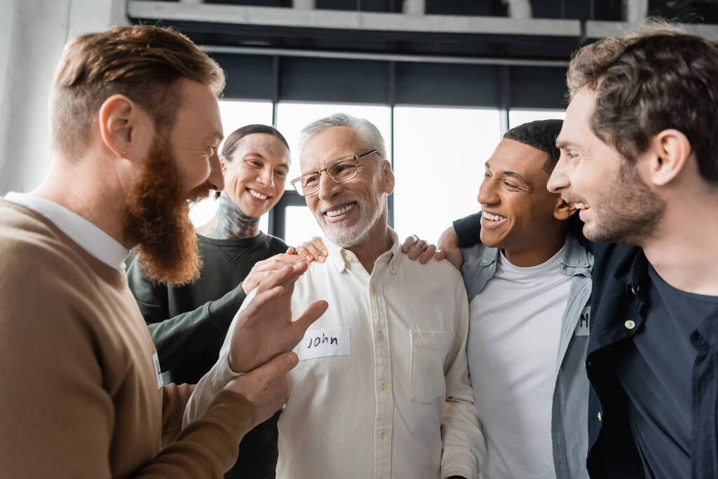 Позитивная мультиэтническая группа обнимает мужчину среднего возраста во время встречи алкоголиков в реабилитационном центре  - Фото, изображение