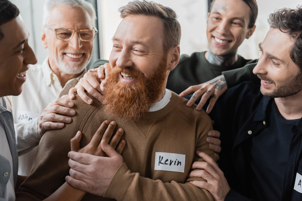 Межрасовые люди обнимают улыбающегося мужчину во время терапии алкоголиков в реабилитационном центре  - Фото, изображение