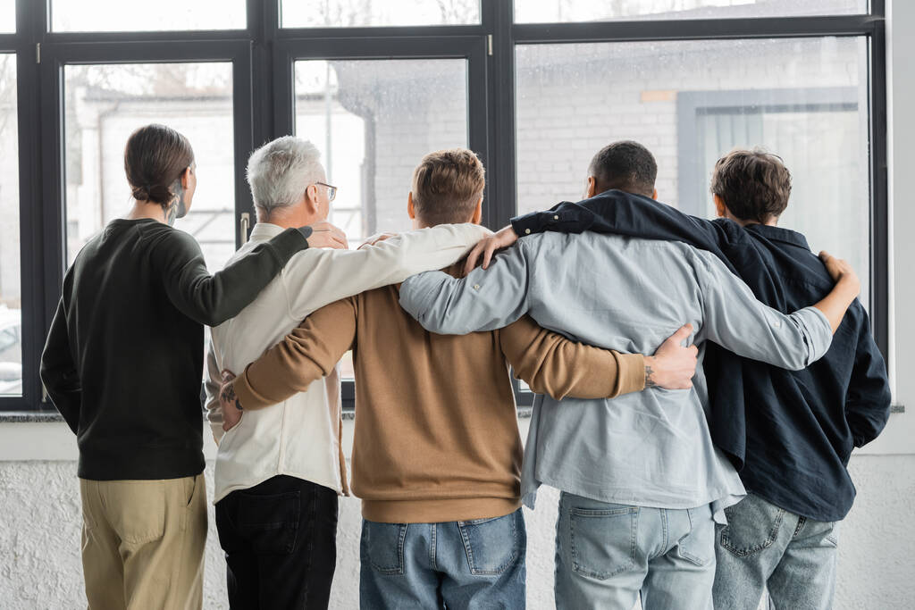 Πίσω όψη των διαφυλετικών ανδρών με εθισμό στο αλκοόλ αγκαλιάζει στο κέντρο αποτοξίνωσης  - Φωτογραφία, εικόνα