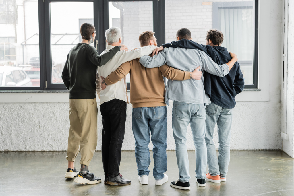 Вид ззаду міжрасових чоловіків, що обіймаються під час анонімної зустрічі алкоголіків у реабілітаційному центрі
  - Фото, зображення