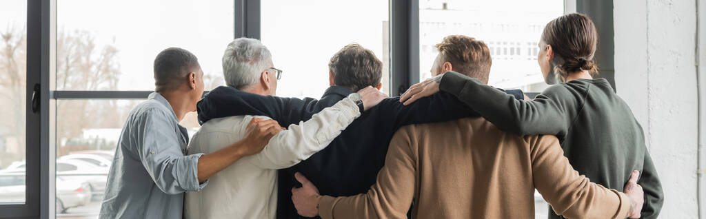 Visão traseira de pessoas inter-raciais abraçando durante a reunião de alcoólicos no centro de reabilitação, banner  - Foto, Imagem