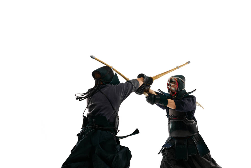 Two men, professional kendo athletes in special uniform training, fighting with shinai sword against white studio background. Concept of martial arts, sport, Japanese culture, action and motion - Photo, Image
