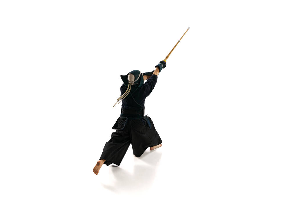 Első látásra. Ember, profi kendo atléta egyenruhában, sisak kiképzéssel, bambusz shinai karddal, fehér stúdió háttérrel. A harcművészet, a sport, a japán kultúra, az akció és a mozgás fogalma - Fotó, kép