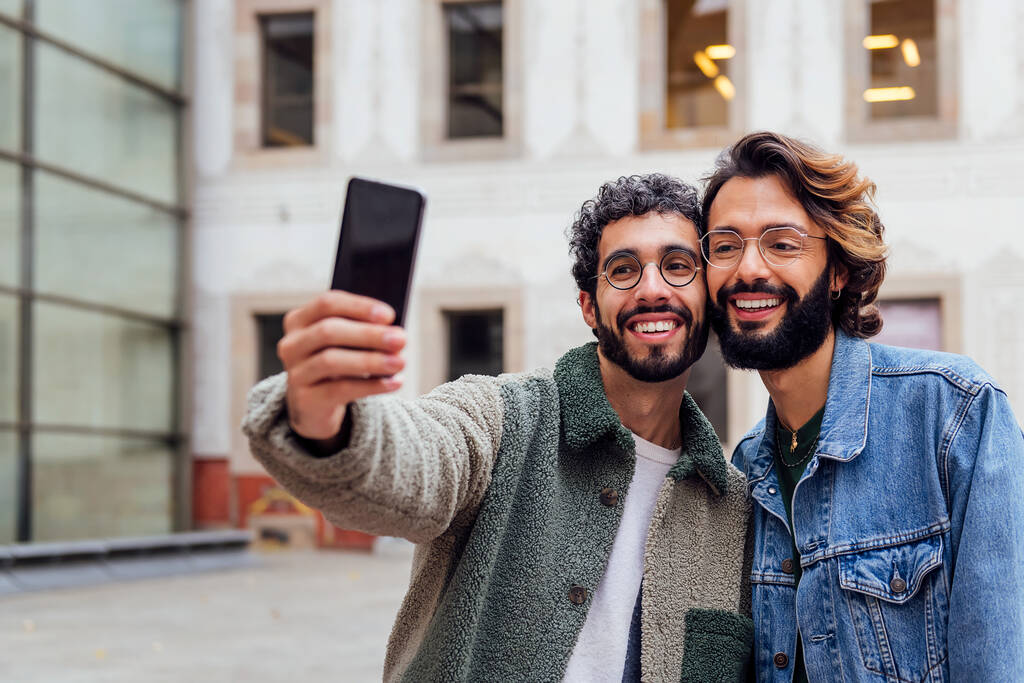 feliz pareja de hombres gay tomando una foto selfie con su teléfono móvil en la calle, concepto de estilo de vida urbano y amor entre personas del mismo sexo, espacio de copia para el texto - Foto, imagen