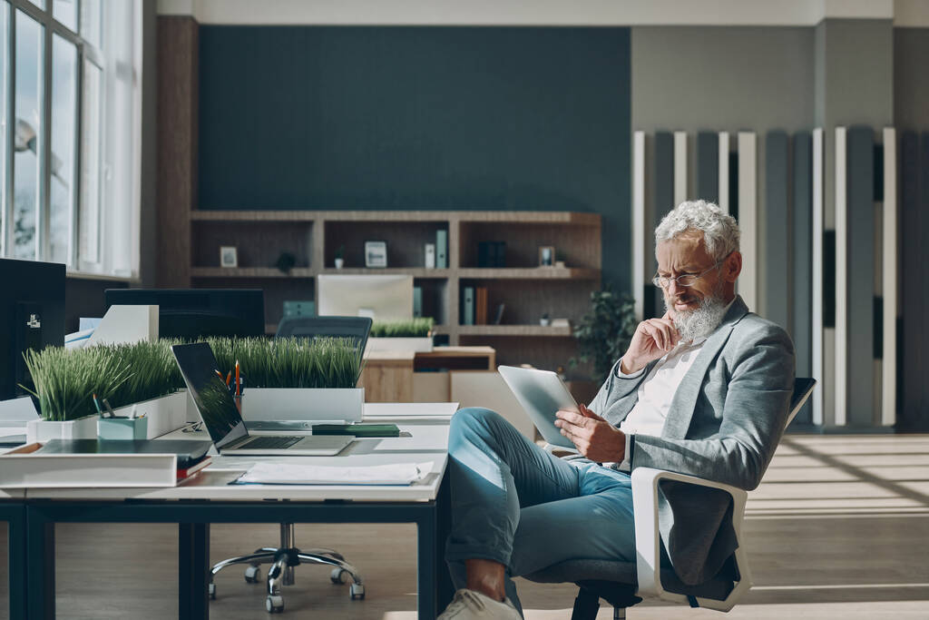 Empresário maduro confiante usando tablet digital enquanto sentado em seu local de trabalho no escritório - Foto, Imagem