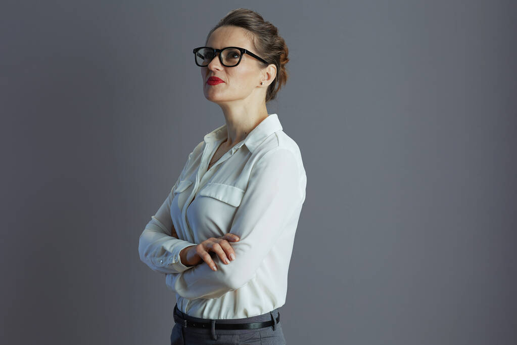 nachdenkliche moderne 40-jährige Geschäftsfrau in weißer Bluse mit Brille auf grauem Hintergrund. - Foto, Bild