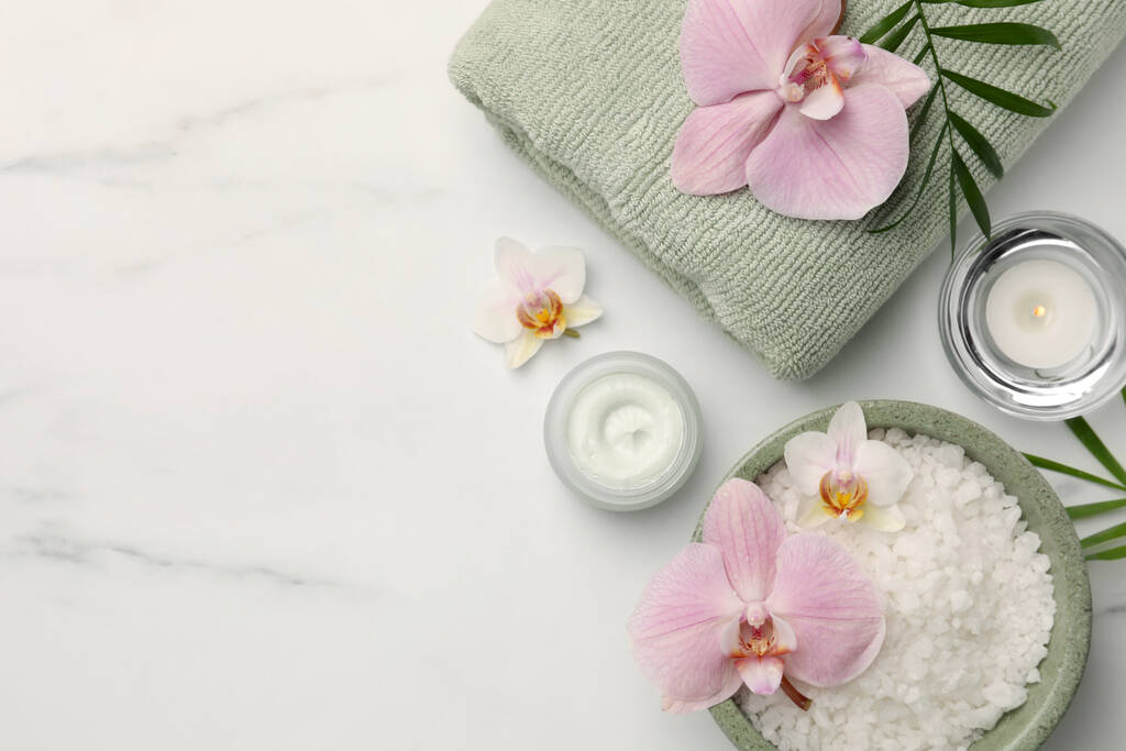 Επίπεδη σύνθεση με διαφορετικά προϊόντα spa και λουλούδια σε λευκό μαρμάρινο τραπέζι. Χώρος για κείμενο - Φωτογραφία, εικόνα