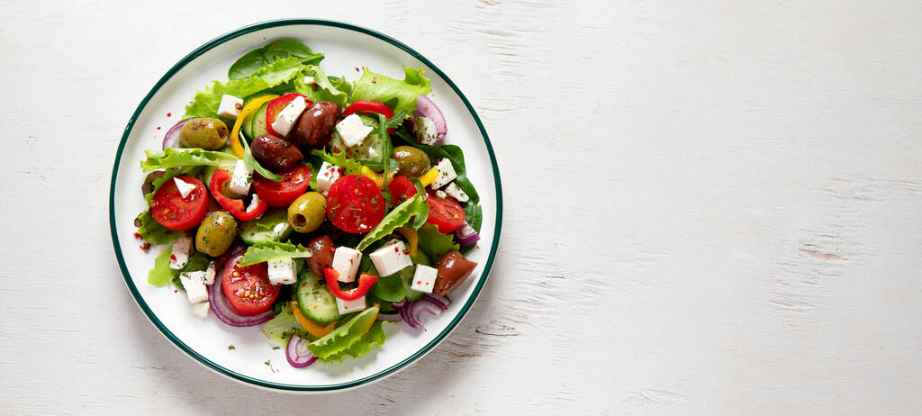 Greek salad of fresh cucumber, tomato, sweet pepper, lettuce, red onion, feta cheese and olives with olive oil on a white background. Healthy food, top view.  Panorama with copy space. - Valokuva, kuva