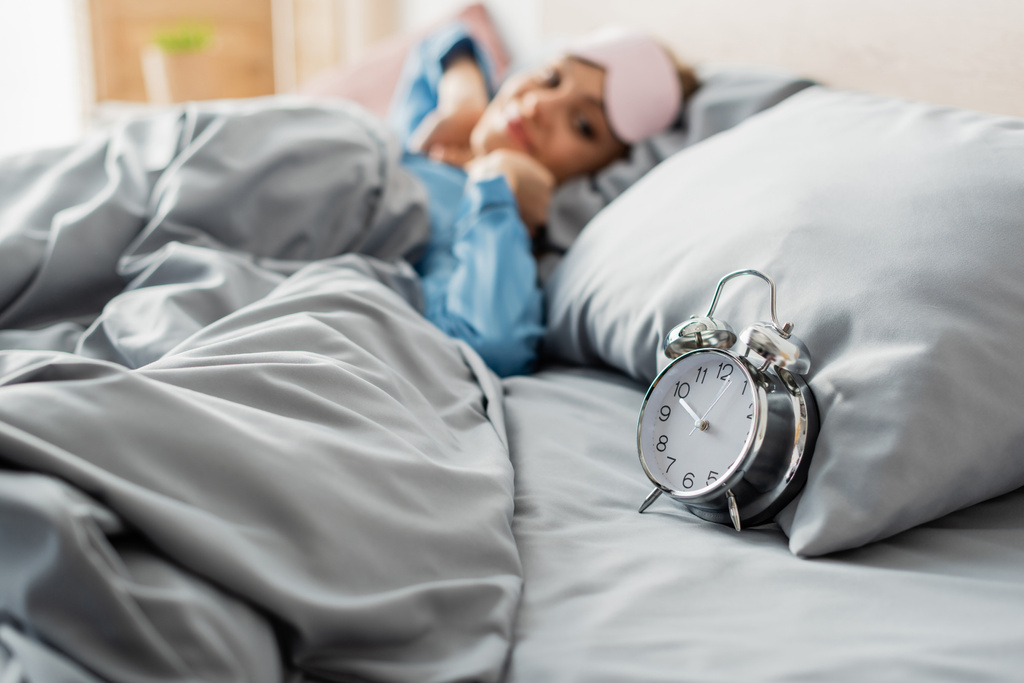 ρετρό ξυπνητήρι στο κρεβάτι σχεδόν ευχαριστημένος γυναίκα σε θολή φόντο  - Φωτογραφία, εικόνα