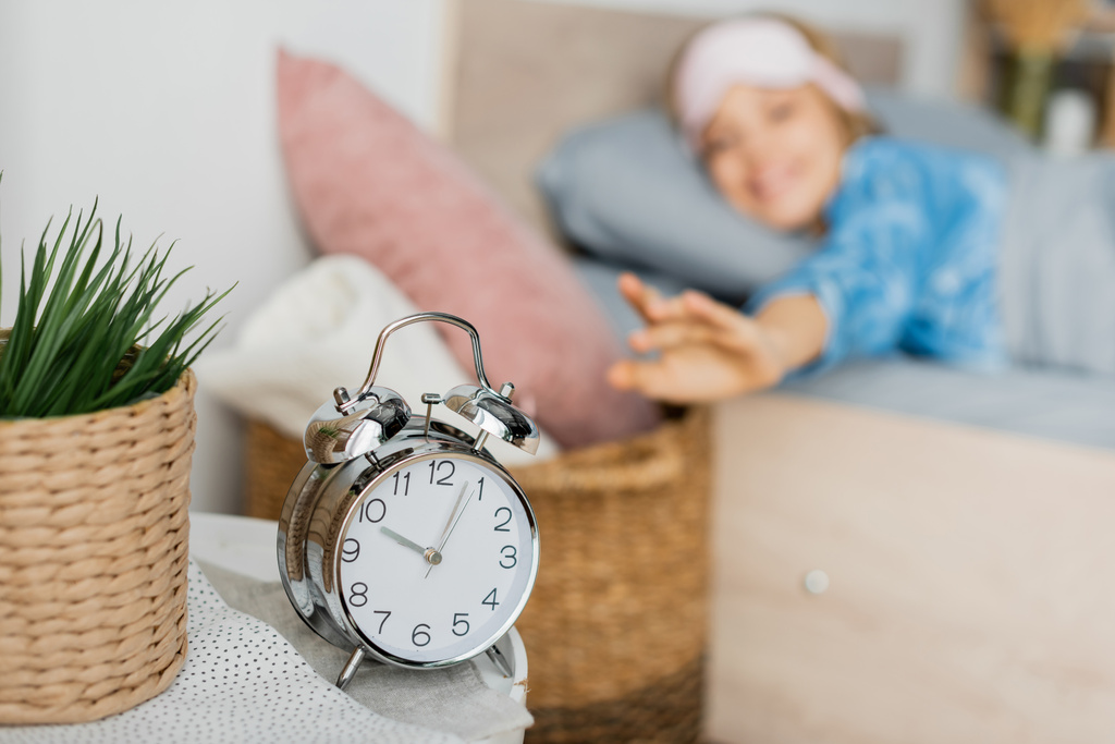 retro despertador na mesa de cabeceira perto de mulher feliz na cama no fundo borrado  - Foto, Imagem