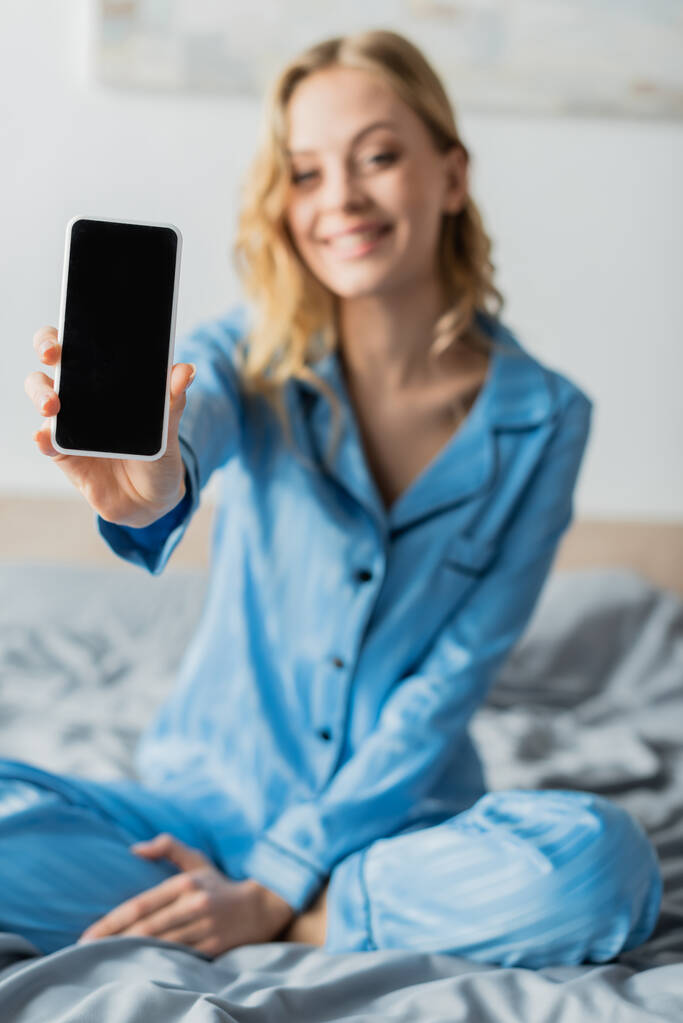 χαρούμενη γυναίκα σε μπλε πιτζάμα κρατώντας smartphone με λευκή οθόνη  - Φωτογραφία, εικόνα