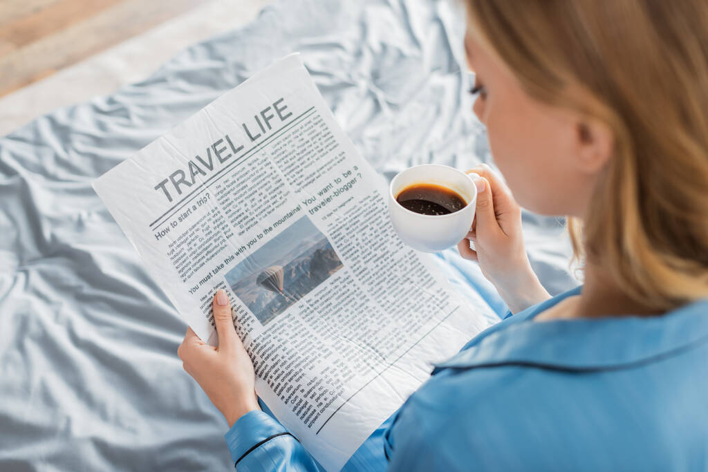 nad głową widok młodej kobiety czytającej dziennik podróży i trzymającej filiżankę kawy w łóżku  - Zdjęcie, obraz
