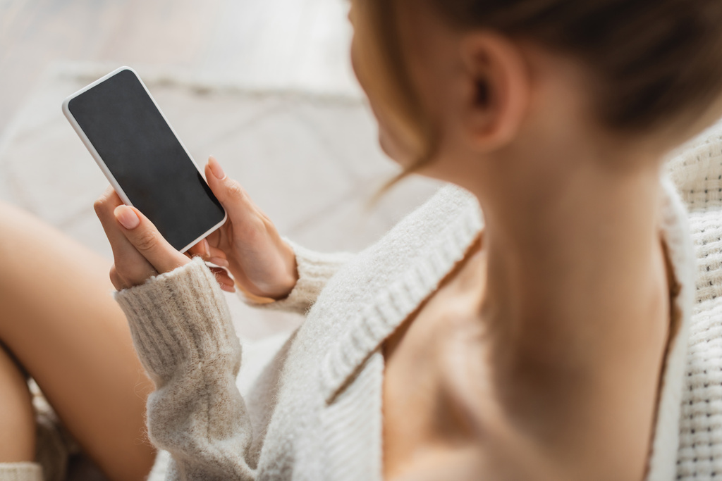 vista aérea de mujer rubia en suéter acogedor usando teléfono inteligente con pantalla en blanco  - Foto, imagen