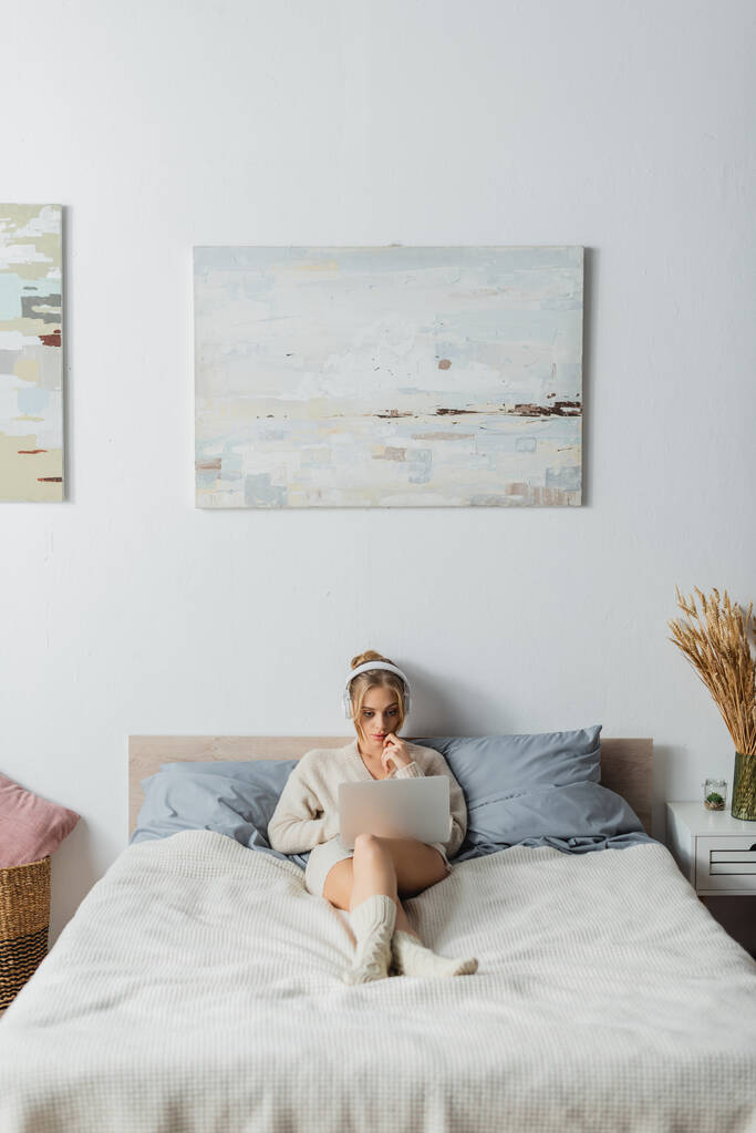 täyspitkä keskittynyt nuori nainen langattomissa kuulokkeissa kannettavan modernin makuuhuoneen  - Valokuva, kuva