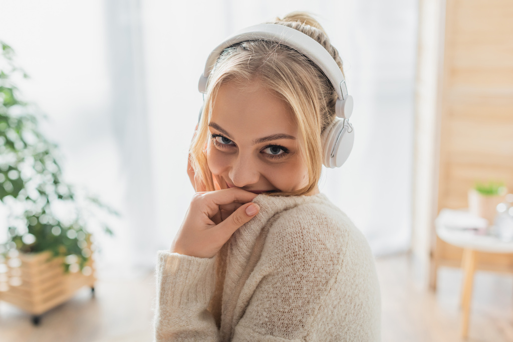 mujer despreocupada escuchando música en auriculares inalámbricos mientras mira a la cámara  - Foto, imagen