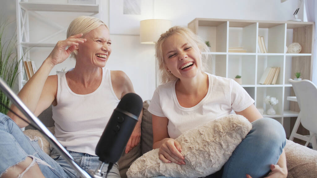 Talk show. Spaß-Podcast. Freizeit zu Hause. Zwei amüsierte Frauen lachen und nehmen Audio-Stream per Mikrofon auf Sofa im Wohnzimmer auf. - Foto, Bild