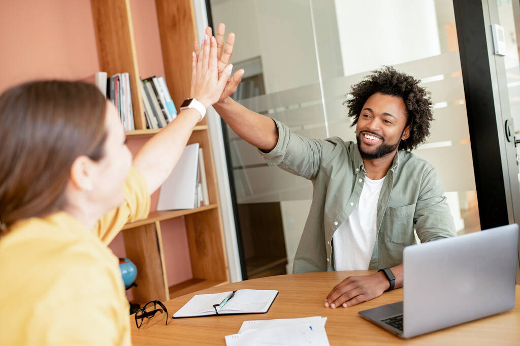 Two diverse employees in smart casual wear giving high five to each other indoors in the contemporary meeting room, celebrating successful collaboration, colleagues support each other - Photo, image