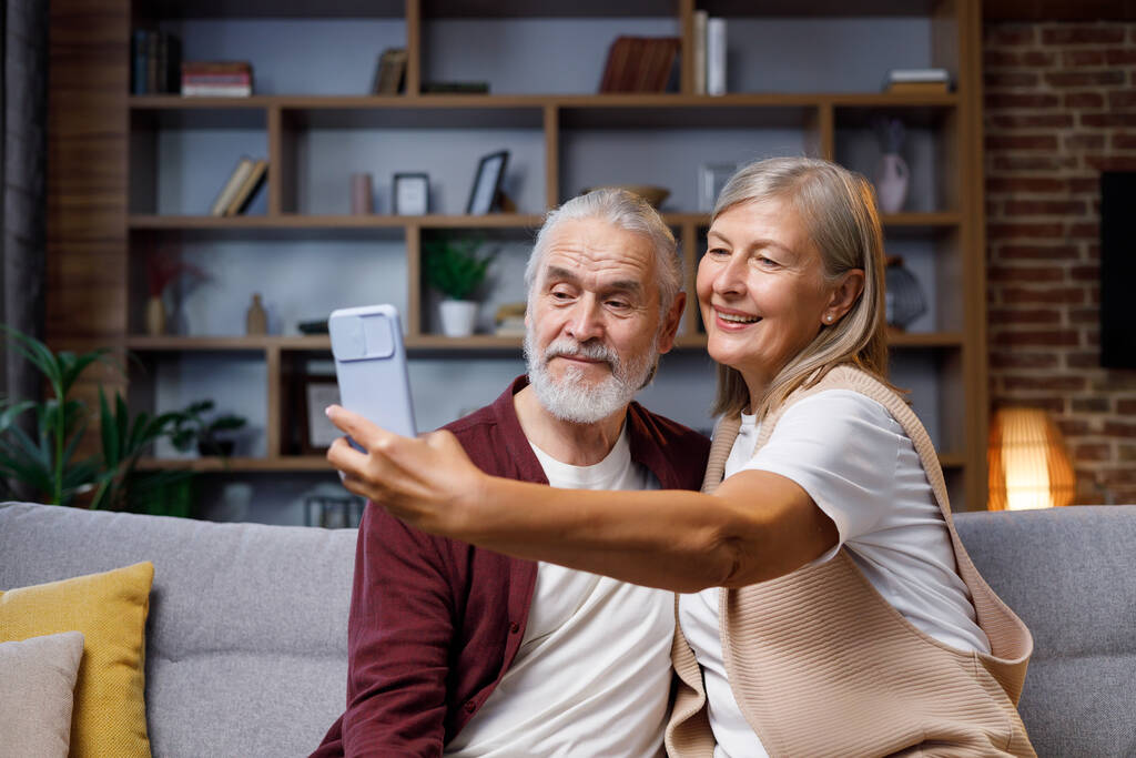 Kypsä onnellinen pari leikkii älypuhelimen kameralla. Harmaahiuksinen mies ja vaimo puhuvat hassuista selfieistä. Videopuhelu älypuhelimella. Onnelliset eläkeläiset - Valokuva, kuva