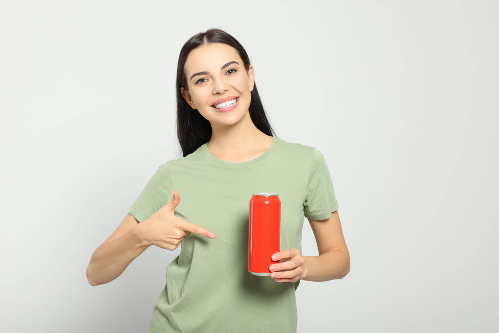 Όμορφη ευτυχισμένη γυναίκα κρατώντας κόκκινο αναψυκτικό μπορεί σε ανοιχτό γκρι φόντο - Φωτογραφία, εικόνα