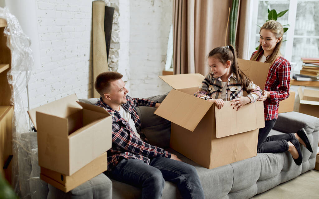 Playful parents and little daughter. Having fun. Young happy family, man, woman and kid moving into new apartment with many cardboard boxes. Concept of moving houses, real estate, family, new life - Photo, Image
