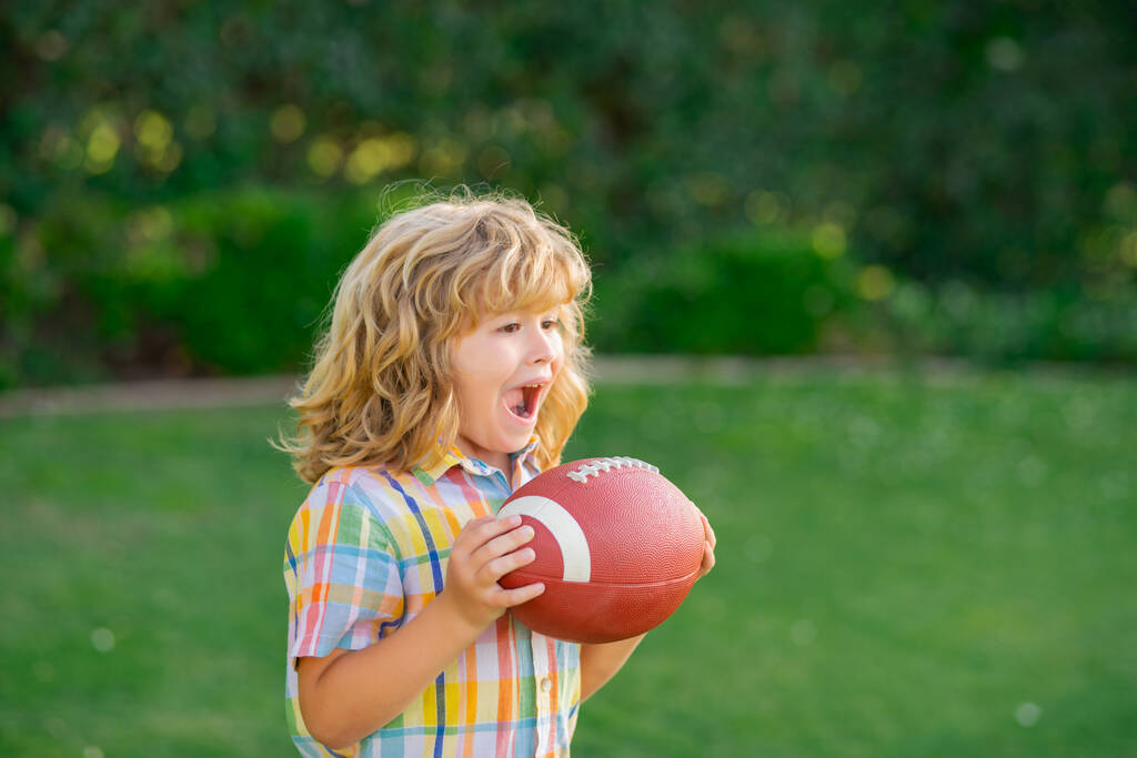Kind mit Rugbyball. Nettes Kind hat Spaß und spielt American Football auf grünem Rasen Park - Foto, Bild