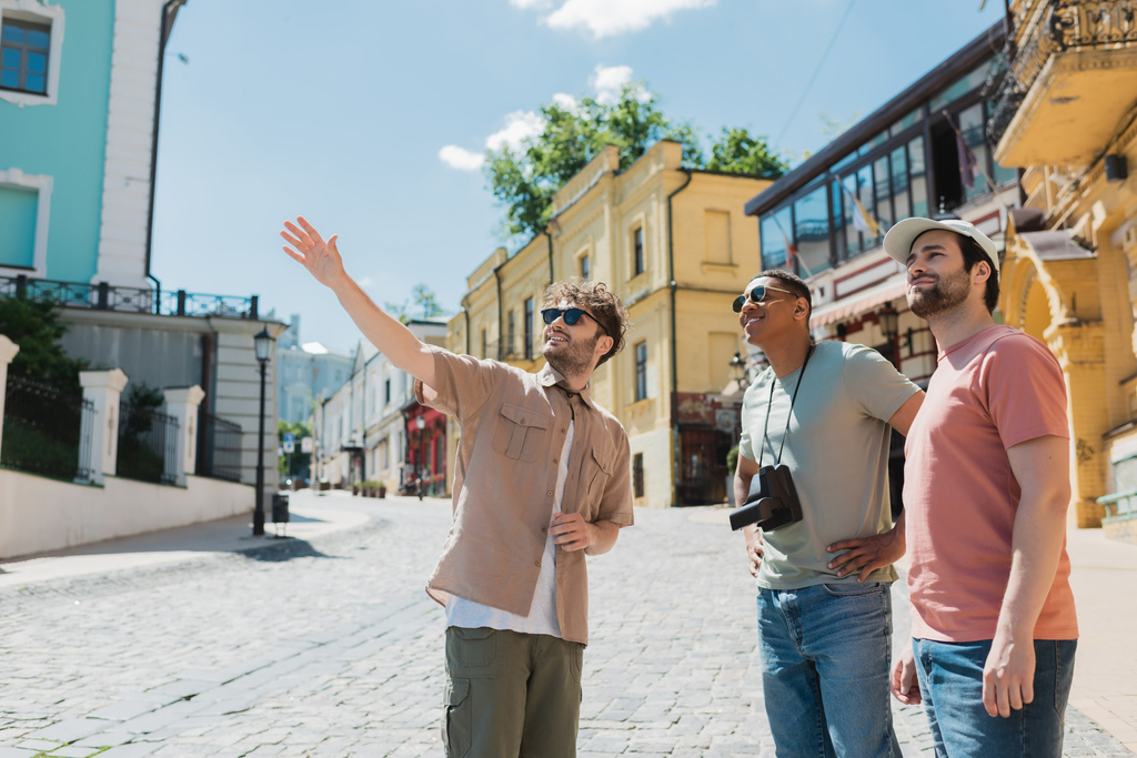 guida turistica in occhiali da sole che punta con mano durante l'escursione con i turisti interrazziale sulla discesa Andrews a Kiev - Foto, immagini
