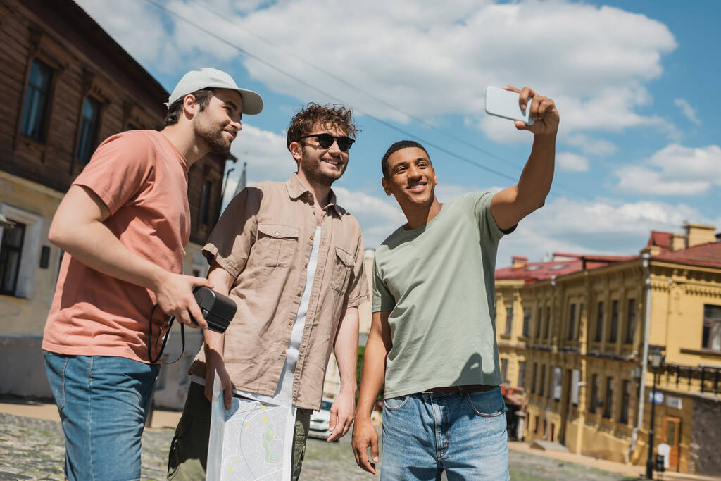 cheerful african american traveler taking photo on smartphone with multiethnic men on Andrews descent in Kyiv - Photo, Image