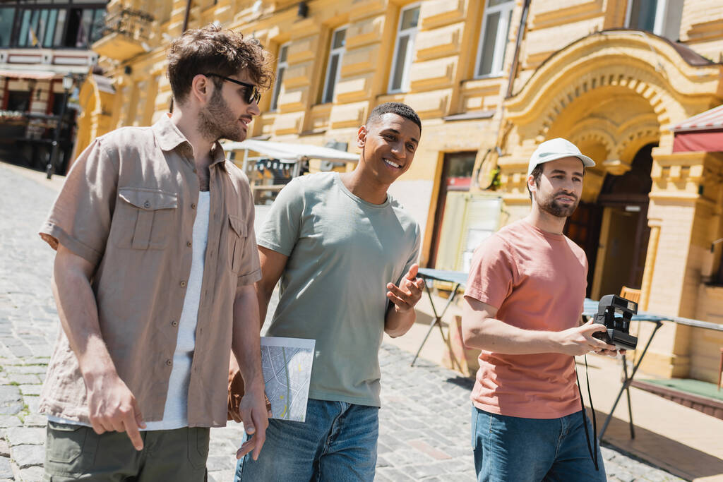 joyeux voyageurs interracial avec carte de la ville et caméra vintage marche avec guide dans les lunettes de soleil sur Andrews descente à Kiev - Photo, image