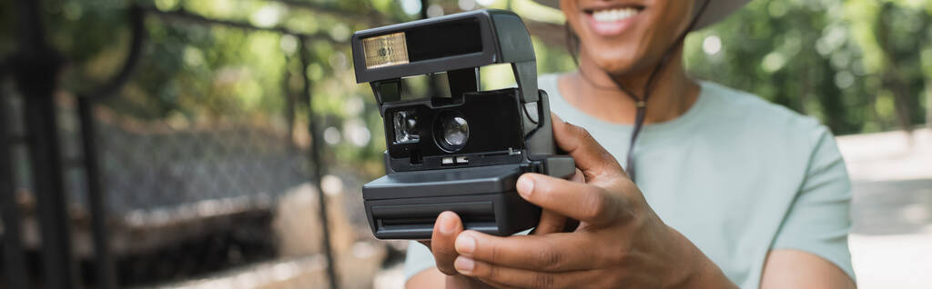 vista parcial del viajero afroamericano borroso con cámara vintage tomando fotos en el parque, pancarta - Foto, Imagen