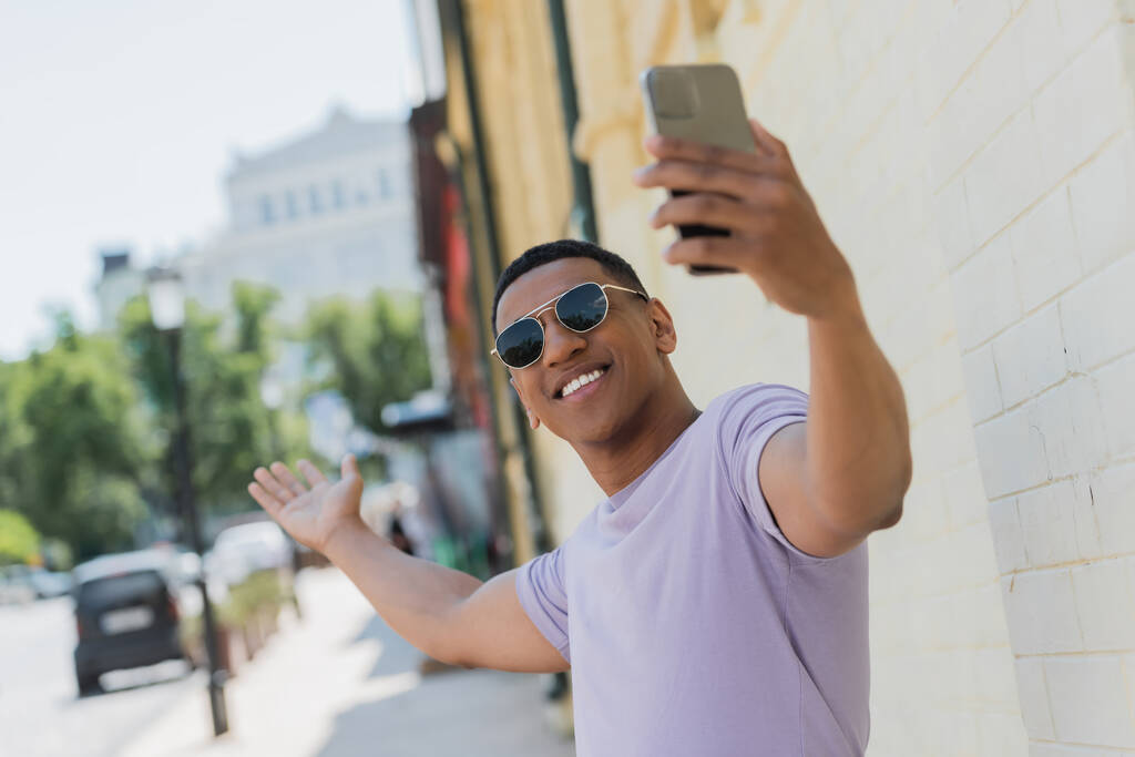 陽気なアフリカ系アメリカ人男性でサングラスをかけてビデオ通話上のスマートフォンでキエフ  - 写真・画像
