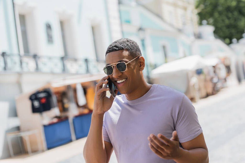 dolblij Afro-Amerikaanse man in een zonnebril praten op mobiele telefoon in de stad straat  - Foto, afbeelding