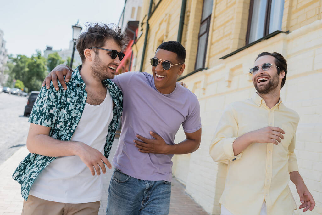 Позитивні міжрасові чоловіки в сонцезахисних окулярах йдуть по Андріївському спуску в Києві.  - Фото, зображення